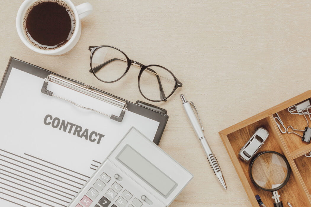 Top view business contract form with coffee eyeglasses car calculator pen with magnifying glass on wooden background.